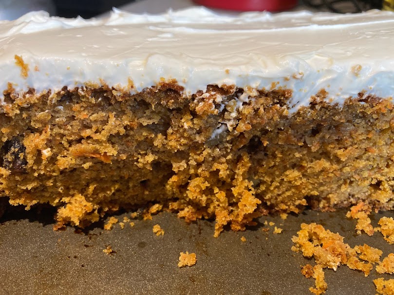 Slice of moist brown sugar carrot cake on at pan, with some delicious crumbs 