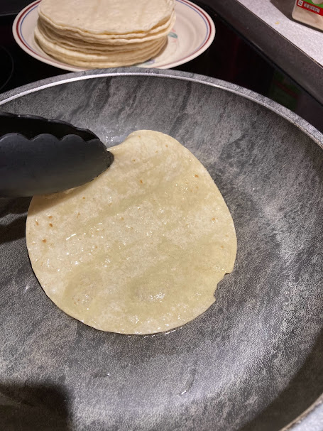 grey saucepan with a lightly fried tortilla being taken off with a tong