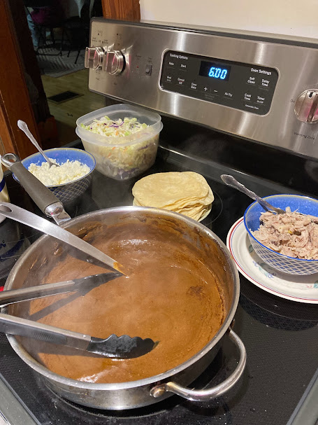 a view of the stovetop, with the hot pot of mole sauce, shredded chicken, tortillas, cabbage, crumbled cheese, ready to be used to assemble the enchiladas