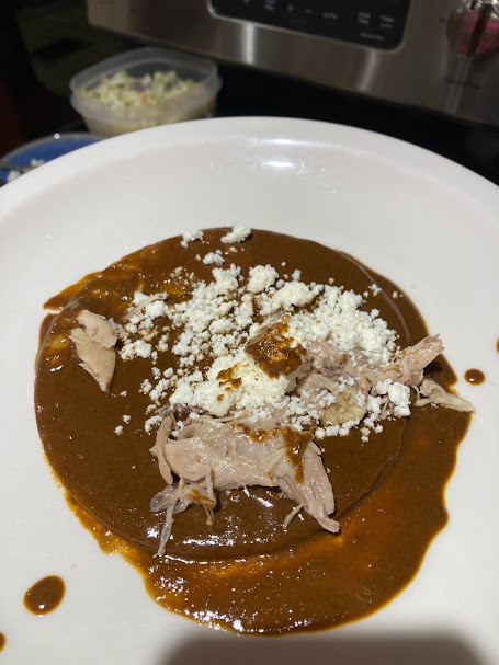 one tortilla dipped in mole sauce on a plate with shredded chicken and cheese in the middle of the tortilla, prior to the tortilla being folded in half