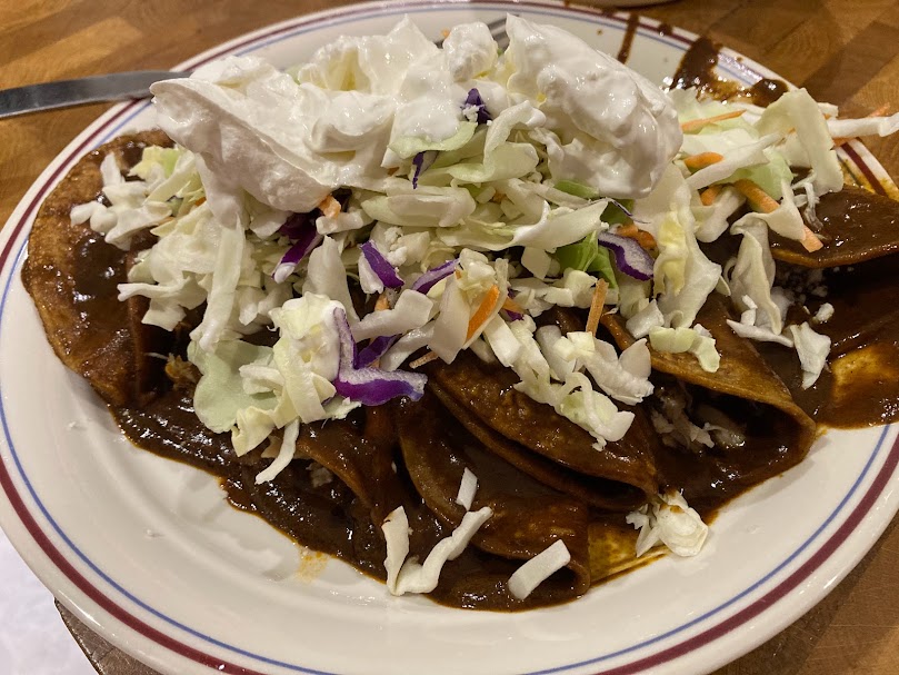 large, delicious plate of enchiladas with a pile of cabbage, crumbled queso fresco and sour cream on top